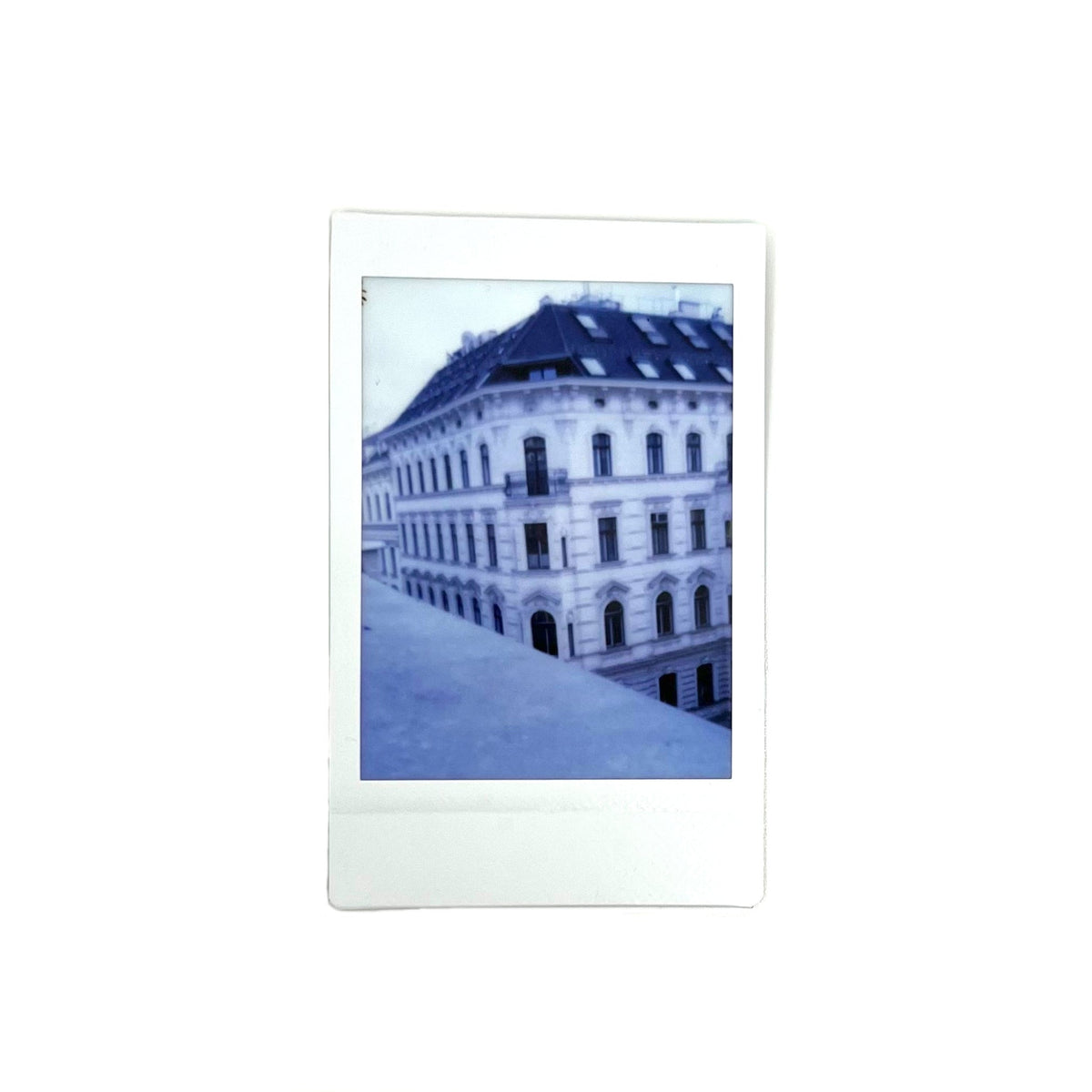 An instant photo taken with a Jollylook Pinhole Mini camera, placed against a white background. The photo features an old building, capturing its unique architectural details and character."