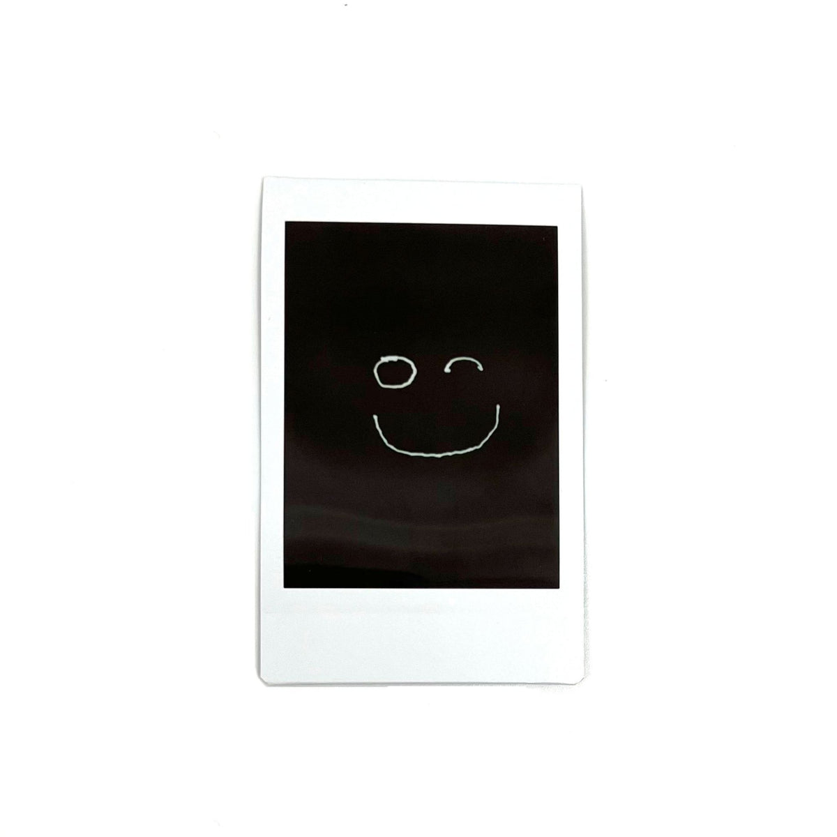 An instant photo captured with a Jollylook Pinhole Mini camera, set against a white background. The photo showcases a smile drawn with light in the darkness, creating a captivating and artistic visual