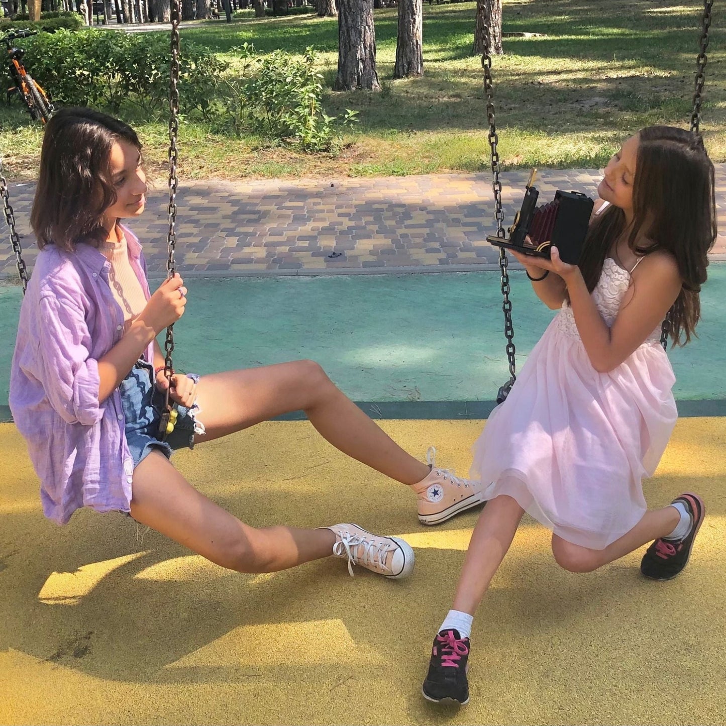 Image featuring the Jollylook Auto Mini Camera in a sleek Ebony Black finish, being used by girls on a swing