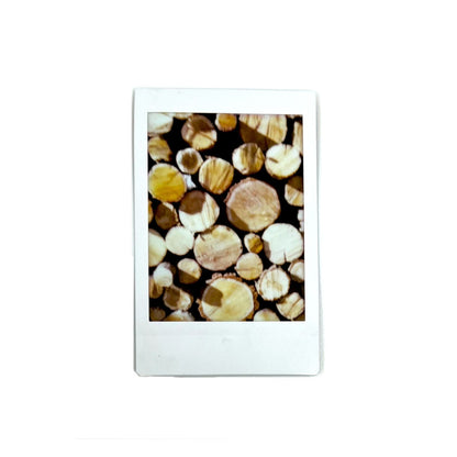 An instant photo captured with a Jollylook Pinhole Mini camera, placed against a white background. The photo showcases a stack of firewood