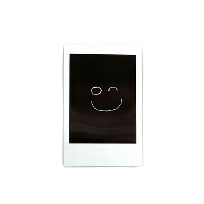 An instant photo captured with a Jollylook Pinhole Mini camera, set against a white background. The photo showcases a smile drawn with light in the darkness, creating a captivating and artistic visual