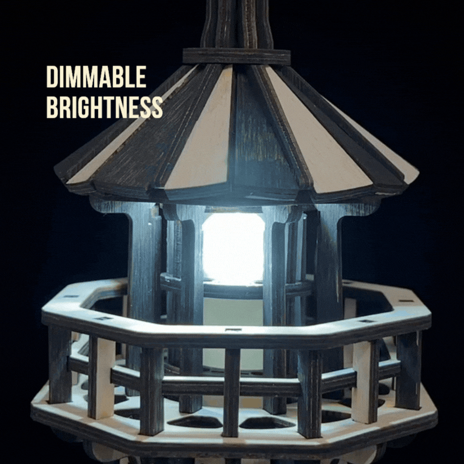 Jollylook Kinetic Lighthouse wooden mechanical model kit assembled and lit on a tabletop. It has a real working light with dimmable brightness.