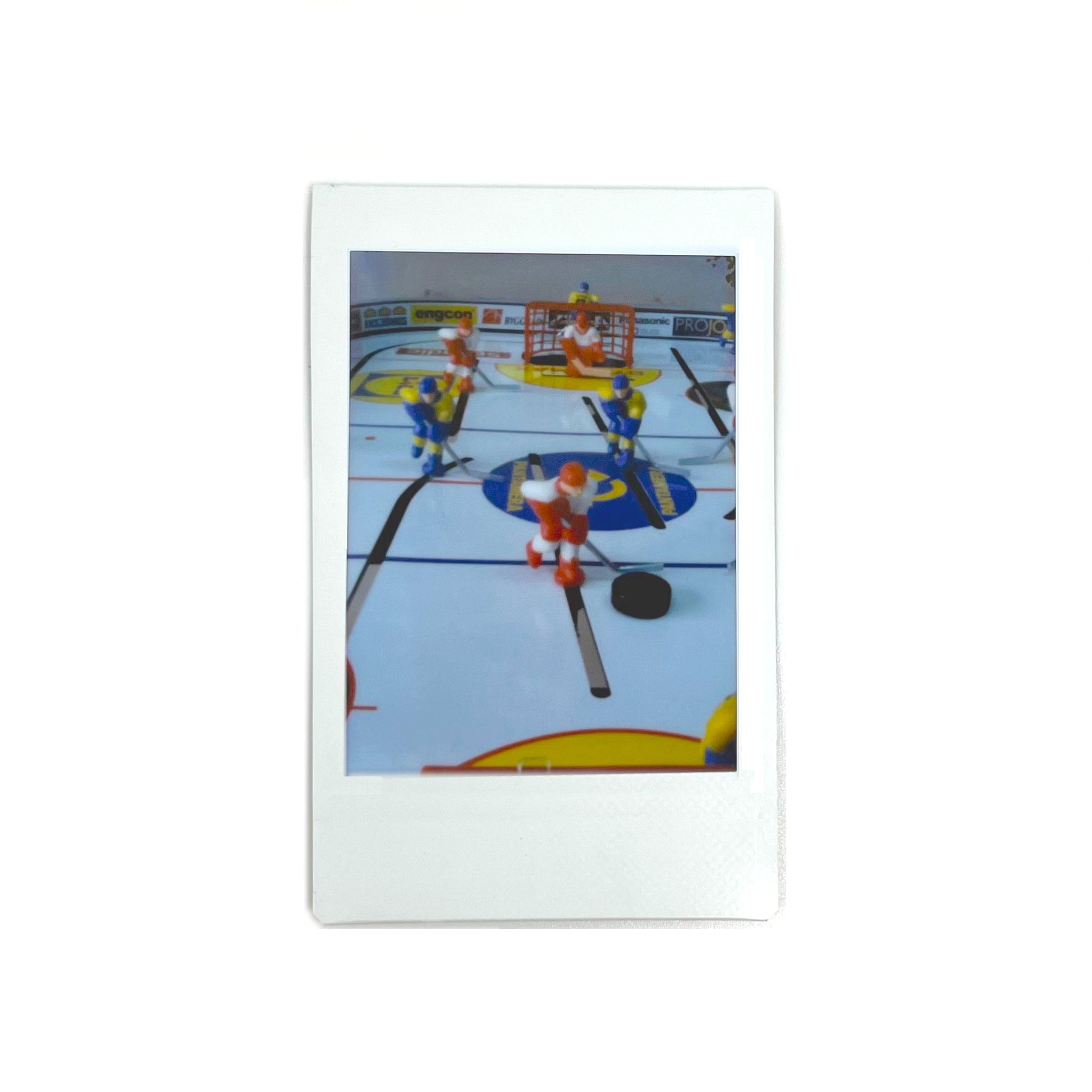 An instant photo taken with a Jollylook Pinhole Mini camera, positioned against a white background. The photo features a table hockey game